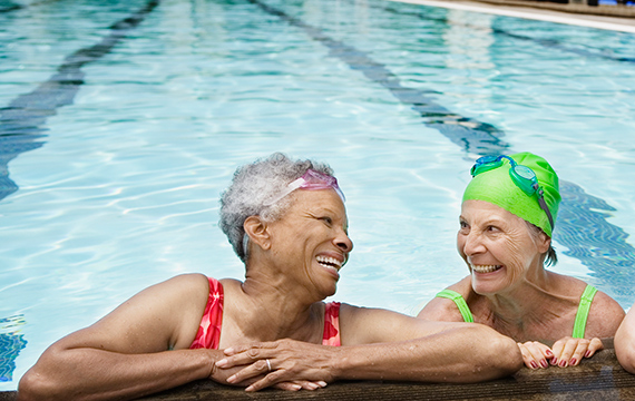 two senior women swimming by the pool