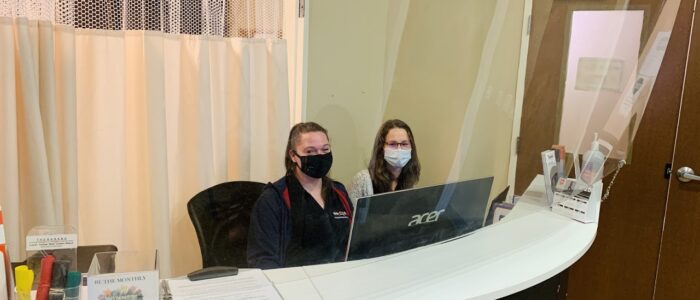 Oshawa Physio clinic showing two receptionists sitting at the reception desk with protective boards